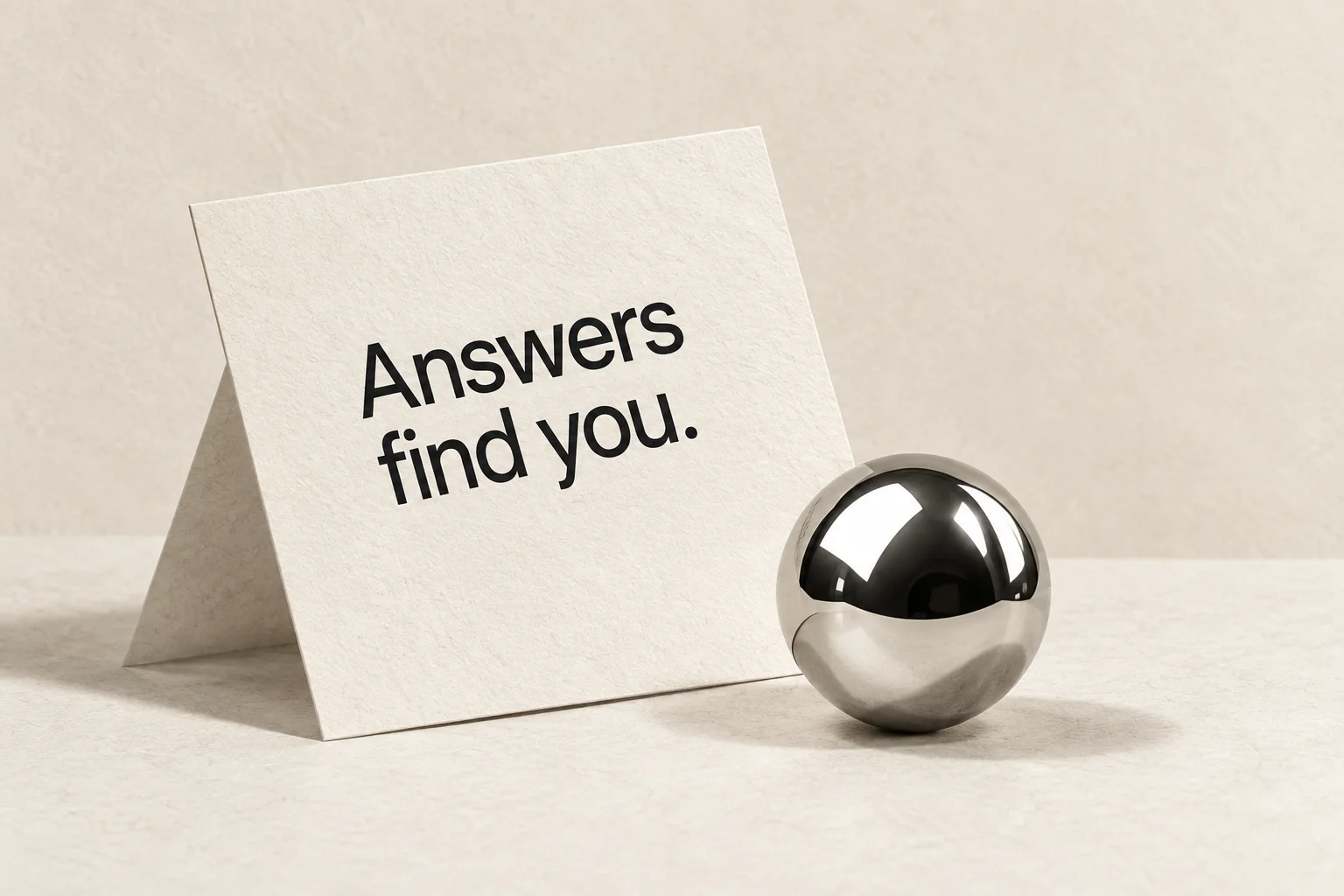 A paper card reading Answers find you beside a chrome sphere