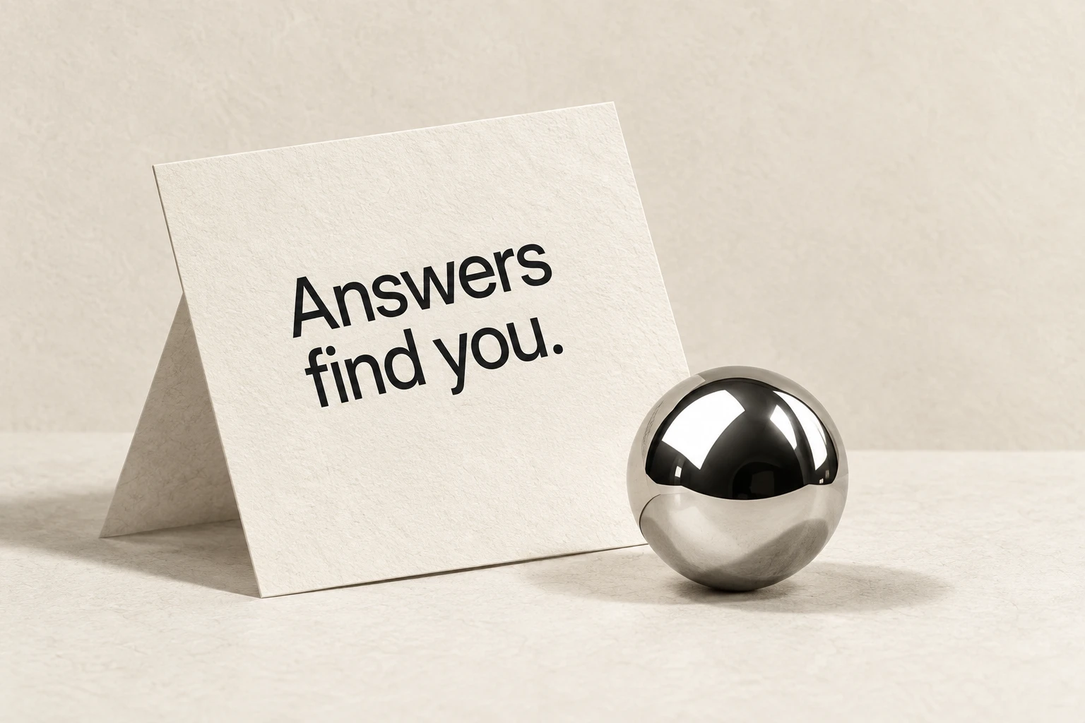 A paper card reading Answers find you beside a chrome sphere